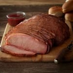 SADLER'S SMOKEHOUSE® sliced beef brisket on a cutting board with buns stacked in the background.