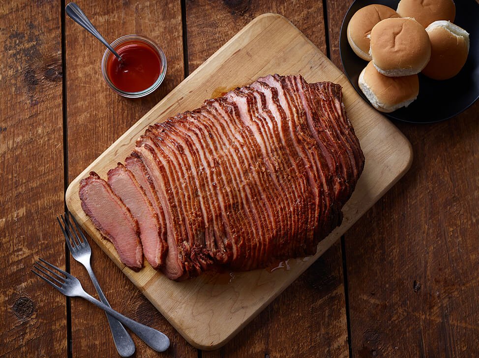 SADLER'S SMOKEHOUSE® sliced beef brisket on a cutting board with buns stacked to the side and a ramekin of bbq sauce.