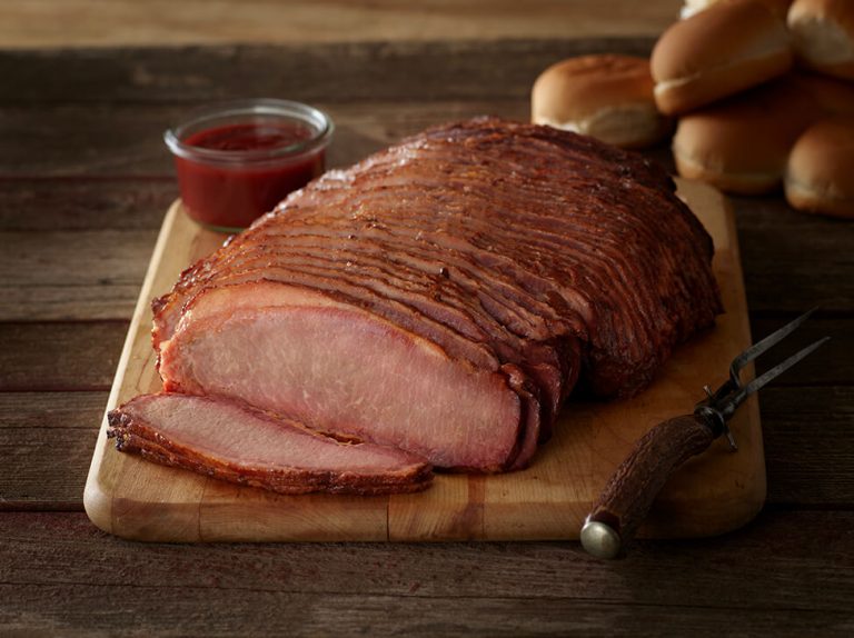 SADLER'S SMOKEHOUSE® sliced beef brisket on a cutting board with buns stacked in the background.