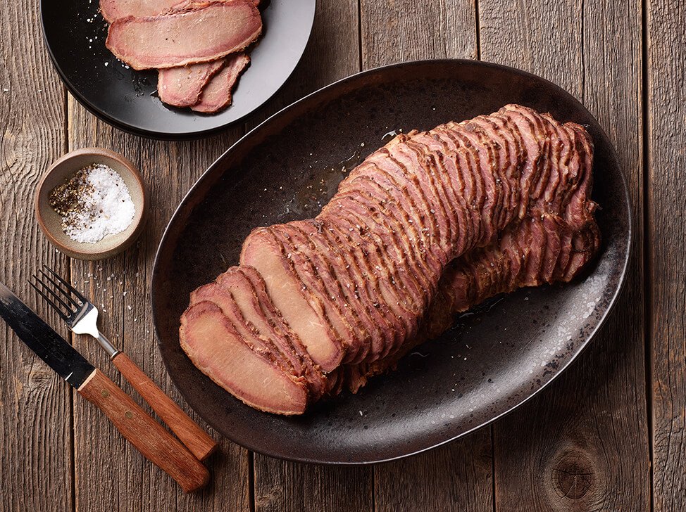 SADLER'S SMOKEHOUSE® TenderSplit beef brisket on a black serving platter with a small plate with brisket slices just off to the side.