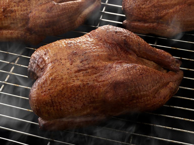 Three SADLER'S SMOKEHOUSE® whole turkeys smoking on a rack.