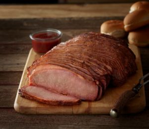 SADLER'S SMOKEHOUSE® sliced beef brisket on a cutting board with buns stacked in the background.