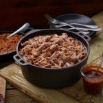 Cast iron pot of SADLER'S SMOKEHOUSE® pulled pork with a cast iron of baked beans behind it.