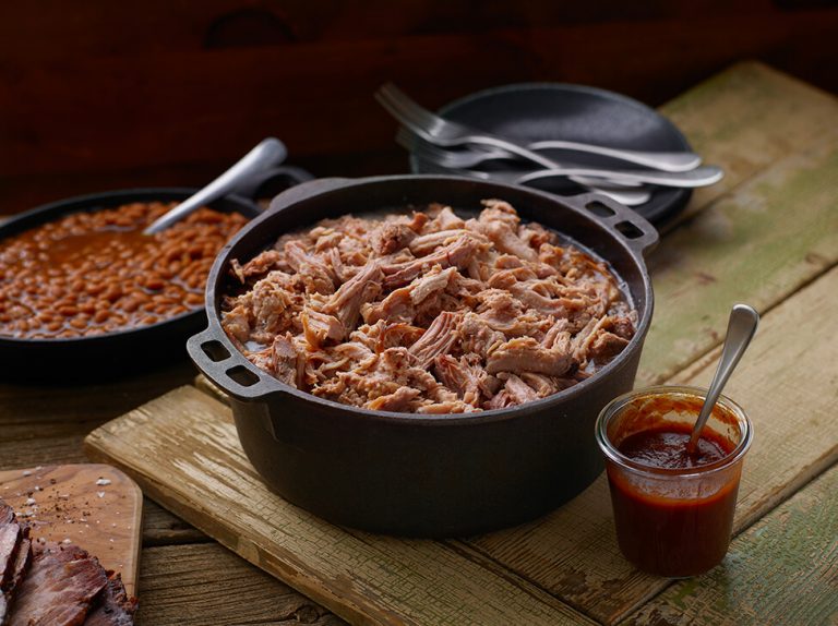 Cast iron pot of SADLER'S SMOKEHOUSE® pulled pork with a cast iron of baked beans behind it.