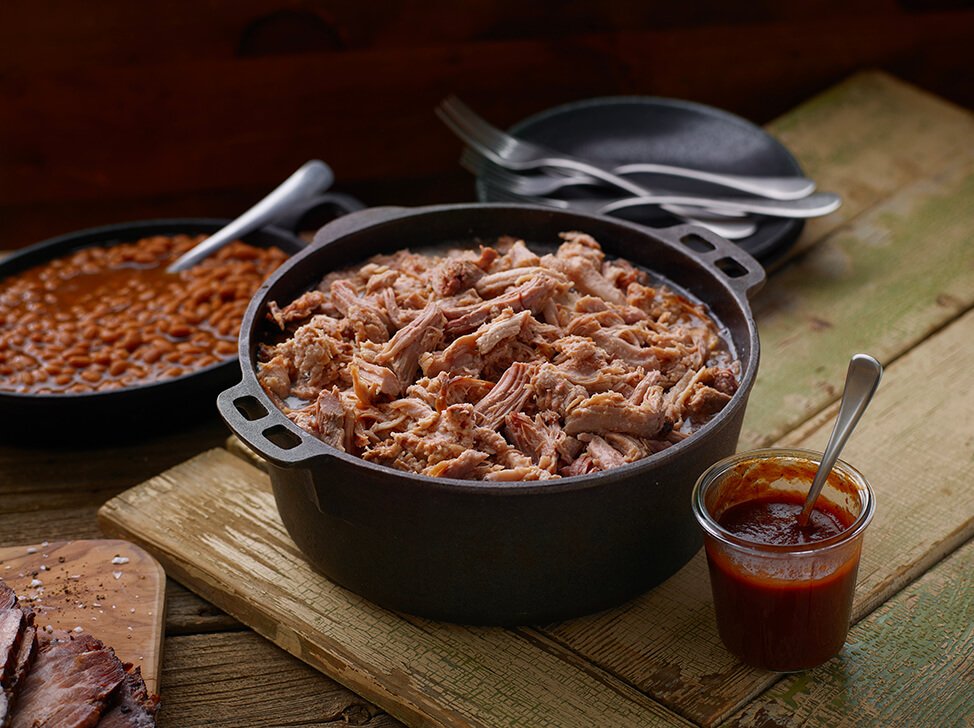 Cast iron pot of SADLER'S SMOKEHOUSE® pulled pork with a cast iron of baked beans behind it.