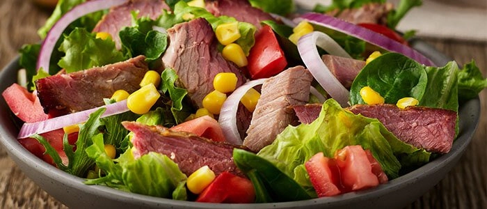 SADLER'S SMOKEHOUSE® brisket on a salad with red onion, corn, and tomato.