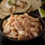 Bowl of Pulled Chicken with tortillas and limes around it.