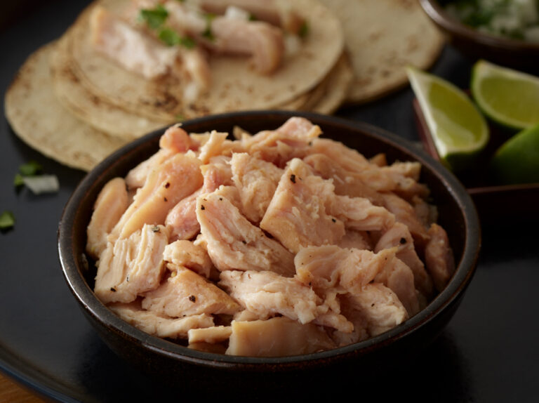 Bowl of Pulled Chicken with tortillas and limes around it.