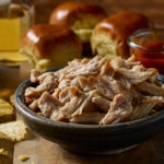 Bowl of pulled chicken with buns and potato chips around the bowl.