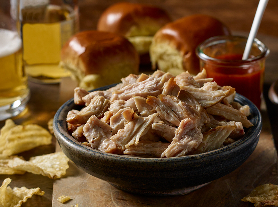 Bowl of pulled chicken with buns and potato chips around the bowl.