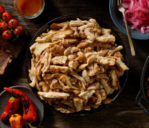 Bowl of pulled chicken with tomatoes, peppers and onions in bowls around it.