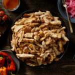 Bowl of pulled chicken with tomatoes, peppers and onions in bowls around it.