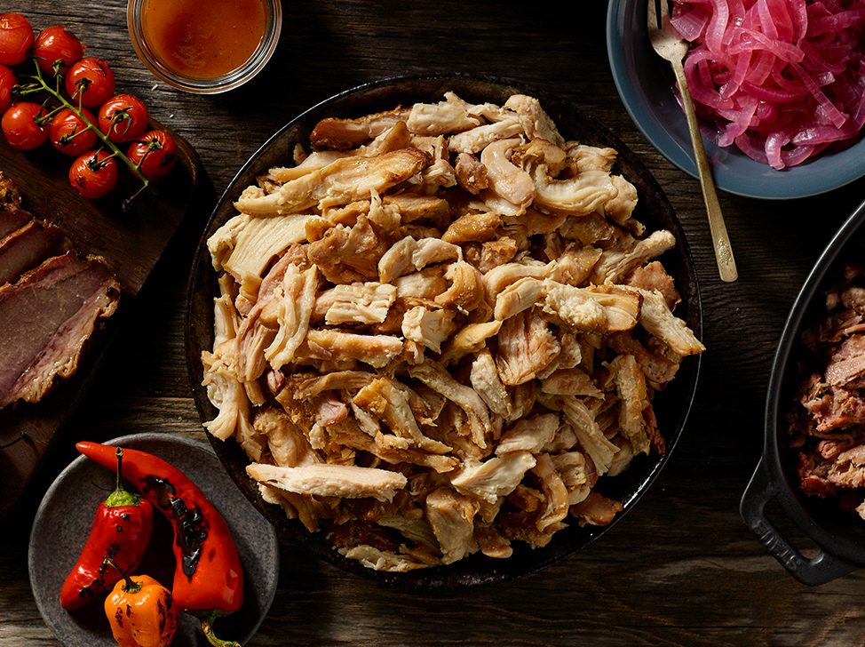 Bowl of pulled chicken with tomatoes, peppers and onions in bowls around it.